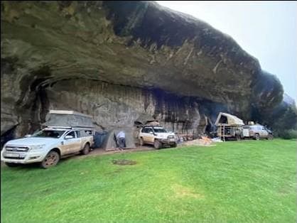 Cave overhang campsite with vehicles and camping setup