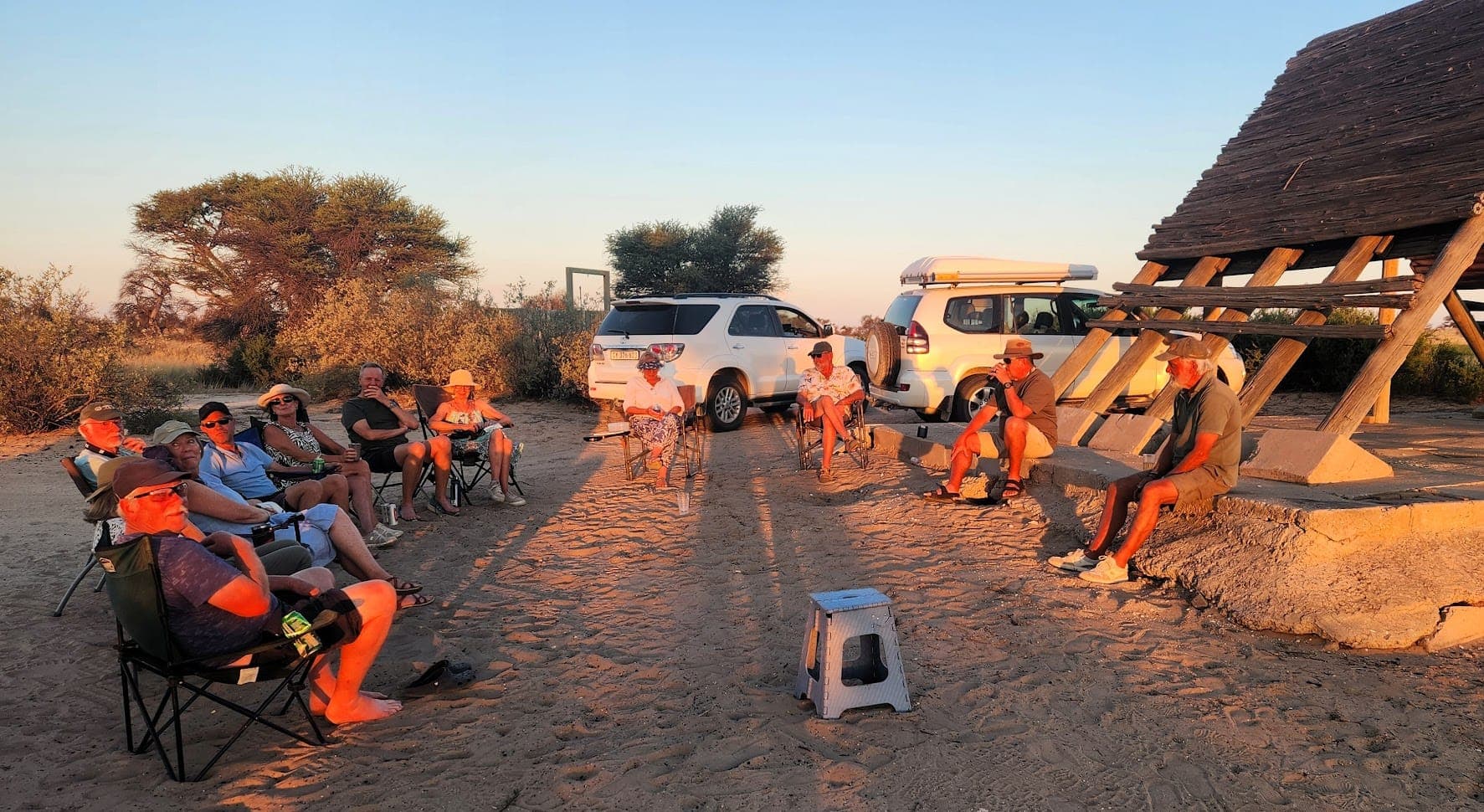 Reisegruppe entspannt in Campingstühlen zur goldenen Stunde mit 4x4-Fahrzeugen