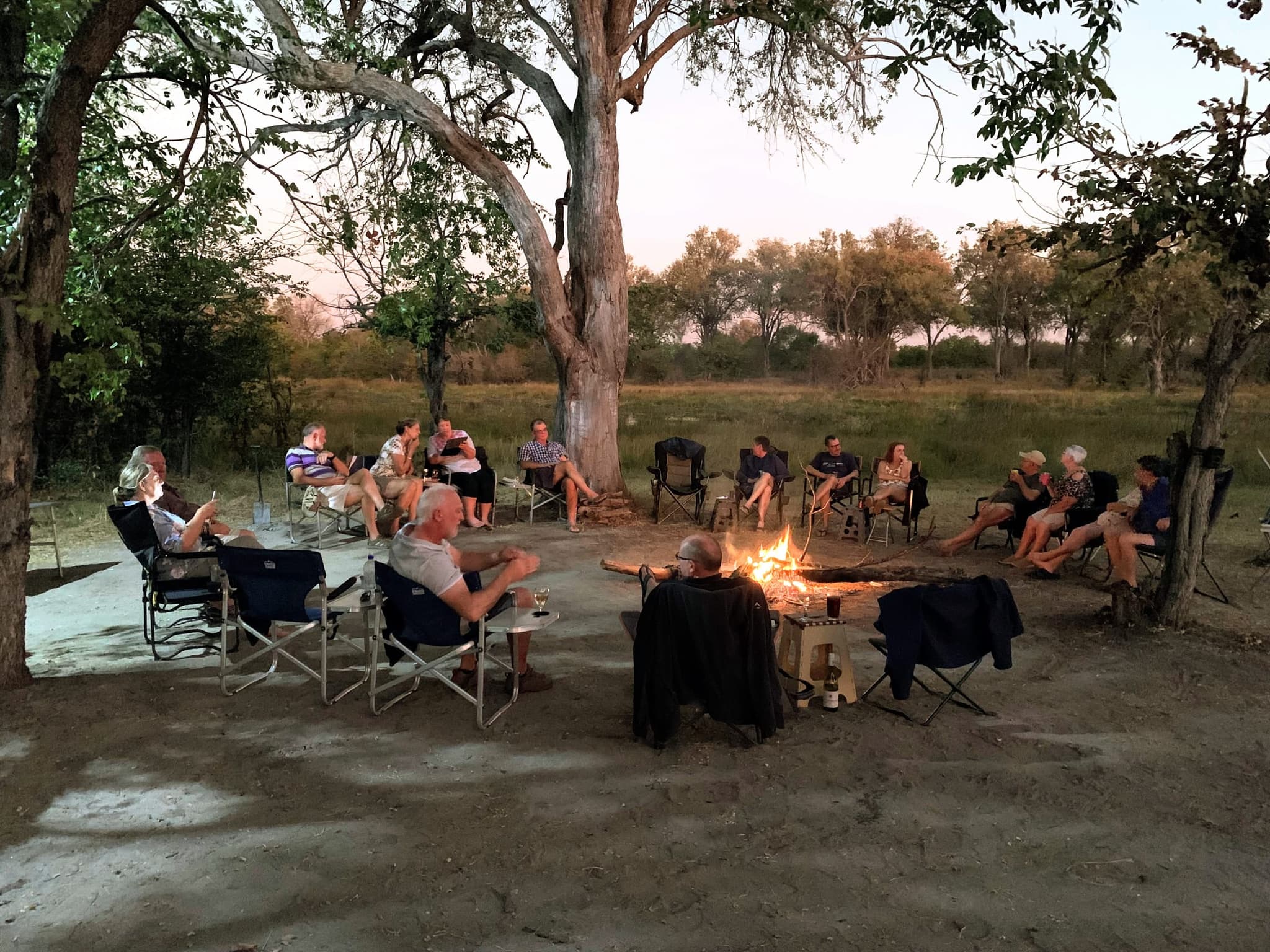 Safari-Gruppe versammelt sich bei Einbruch der Dunkelheit um ein Lagerfeuer im afrikanischen Busch