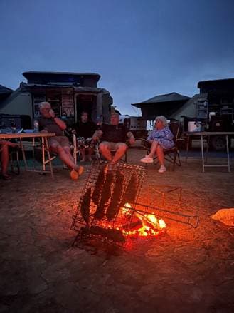 Traditioneller südafrikanischer Braai am Lagerfeuer in der Abenddämmerung mit Gruppe, die den Abend genießt