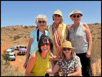 Gruppe von Abenteurern posiert in der Kalahari-Wüste mit 4x4-Fahrzeugen im Hintergrund