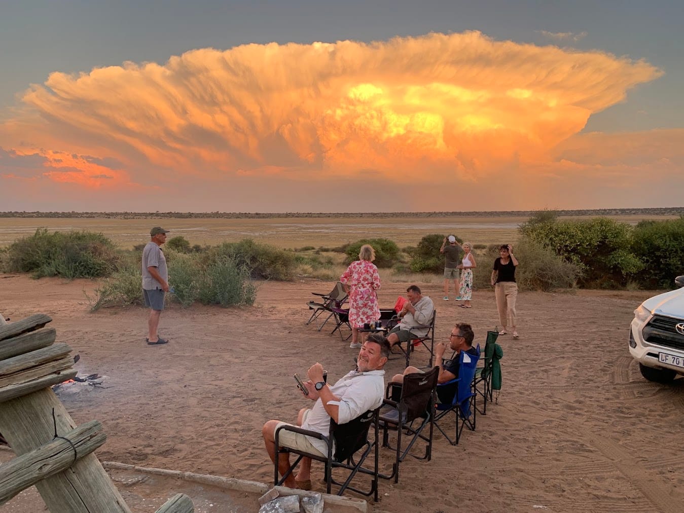 Gruppe entspannt im Camp mit dramatischen goldenen Gewitterwolken bei Sonnenuntergang in der Kalahari