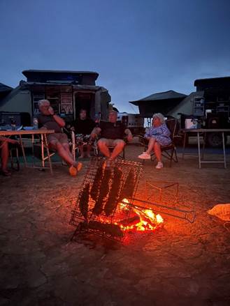 Traditioneller südafrikanischer Braai am Lagerfeuer in der Abenddämmerung mit Gruppe, die den Abend genießt